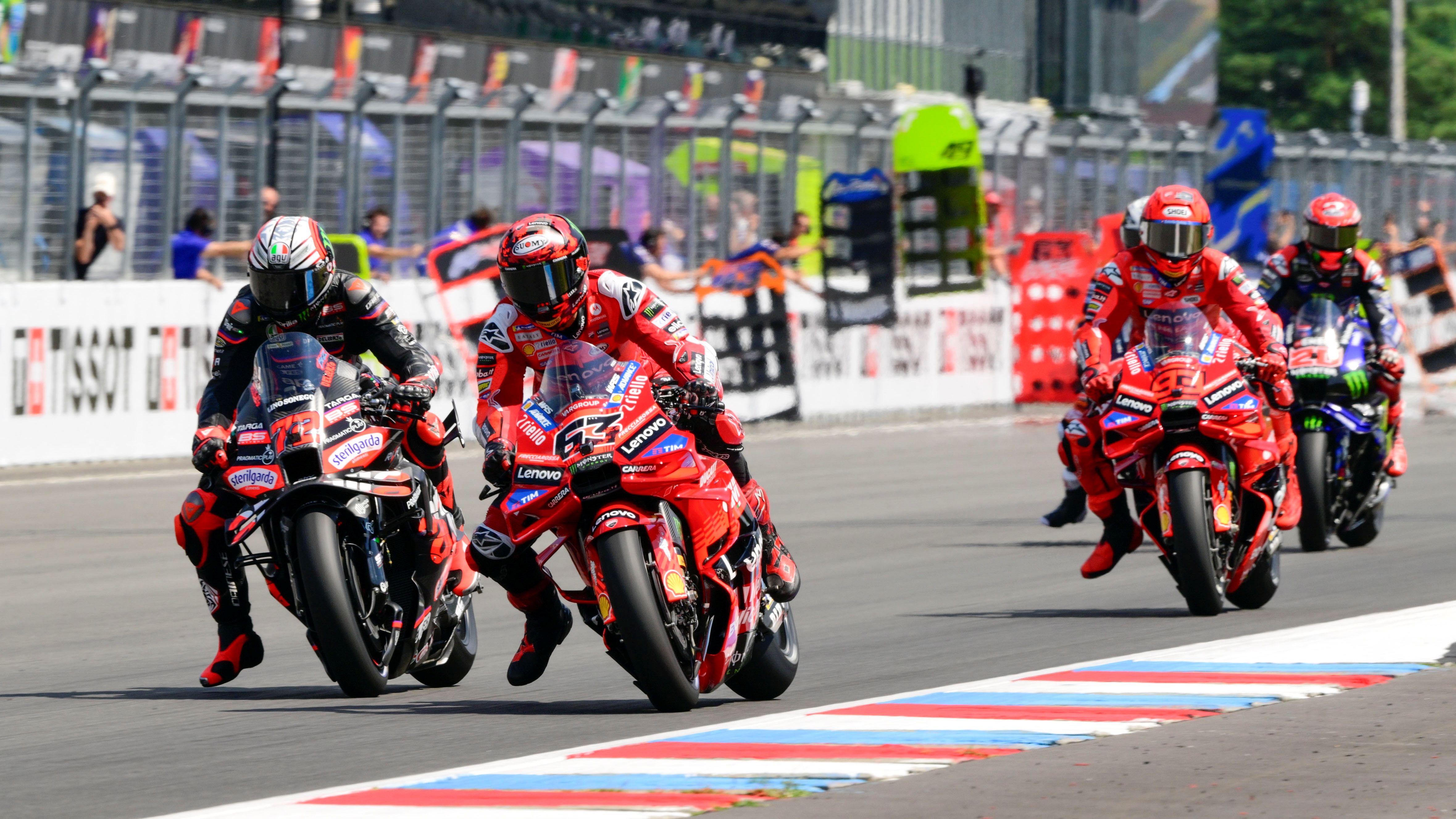 Marco Bezzecchi busca el interior de Pecco Bagnaia ante la presencia de Marc Márquez, MotoGP Chequia 2025