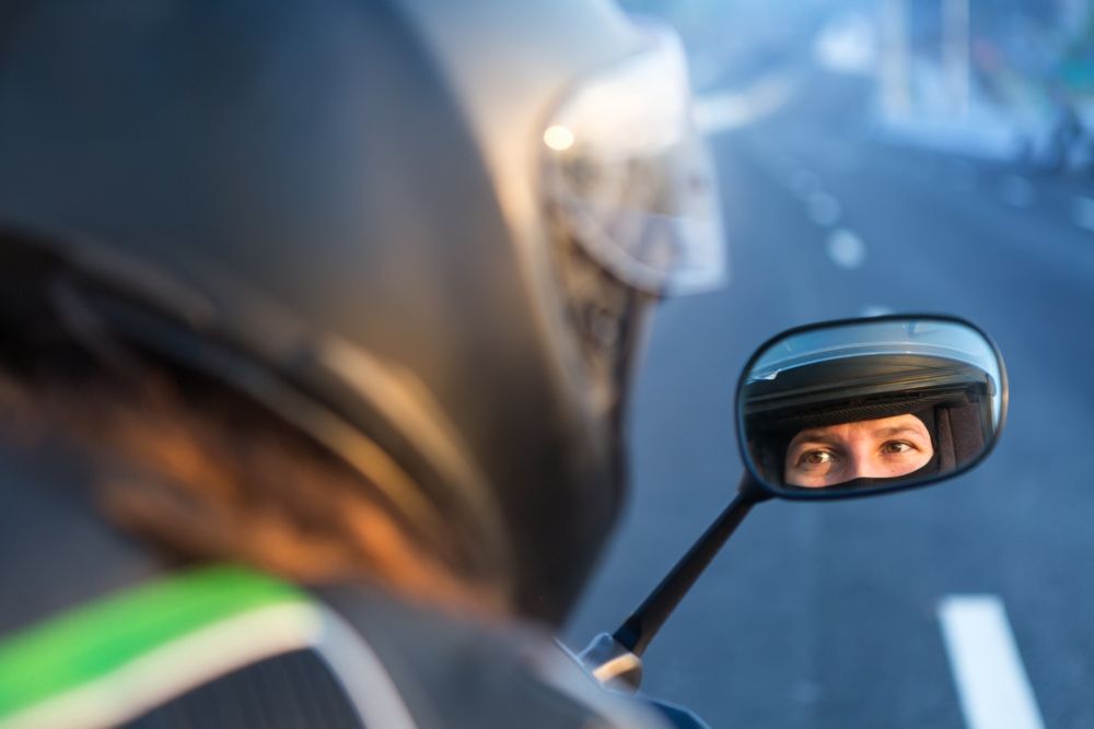 Motorista mirando a través de uno de los espejos de su moto. Fuente : iStock / jkitan