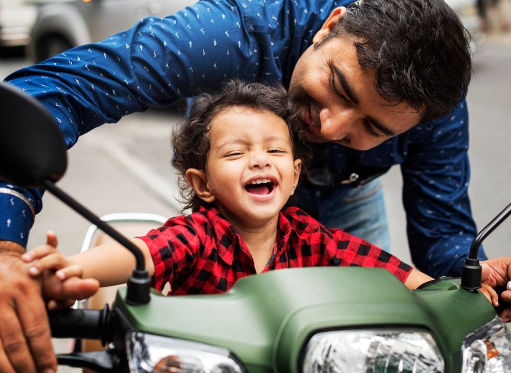 Niño subido a la moto de su padre, la réplica real de su correpasillos. Fuente: iStock / Rawpixel 