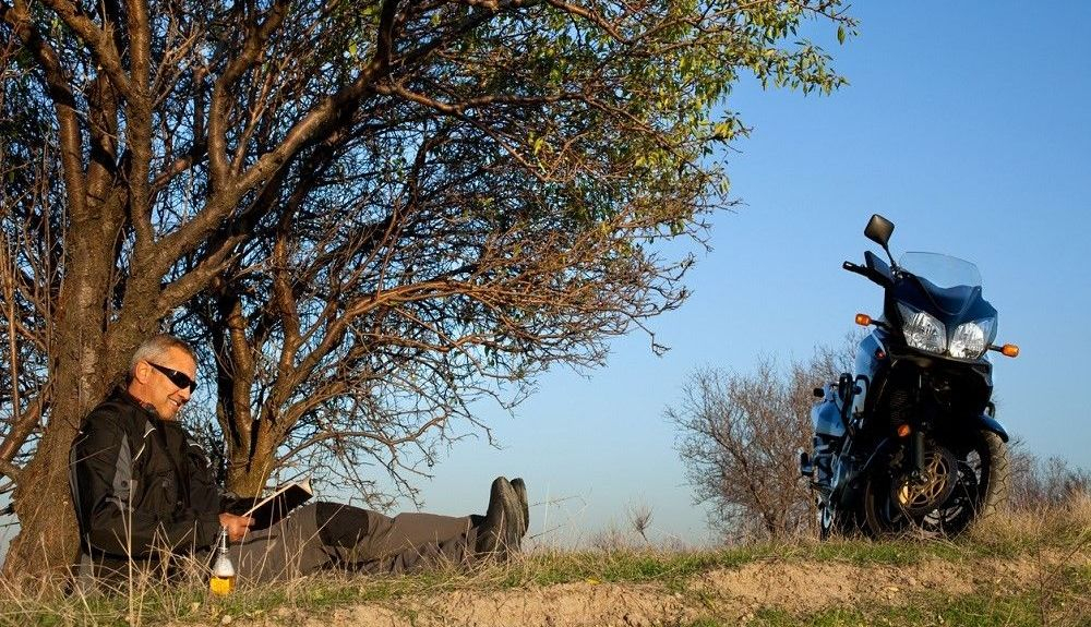 Hombre leyendo junto a su moto. Fuente: iStock/usas